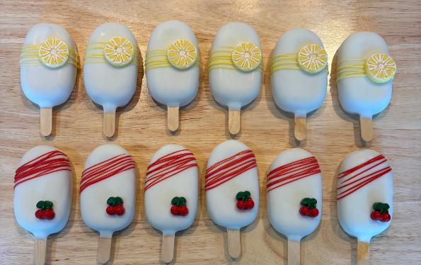 White cakesicles with lemon slice toppers and cherry drizzle designs